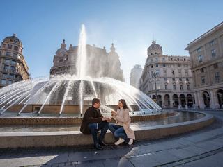 Un couple profite d'un moment près de la fontaine de la Piazza de Ferrari, entouré de bâtiments historiques à Gênes, Italie | MSC Croisières