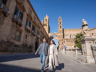 Ein Paar spaziert gemeinsam auf einem historischen Platz mit einer Kathedrale und einem Bogen im Hintergrund unter einem klaren blauen Himmel | MSC Cruises