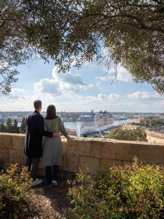 Un couple profite d'une vue panoramique sur La Valette depuis les jardins Barrakka, avec des bateaux dans le port et des arbres autour d'eux | MSC Croisières