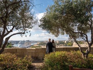 A couple enjoys a panoramic view of Valletta and the sea from Barrakka Gardens, surrounded by trees | MSC Cruises