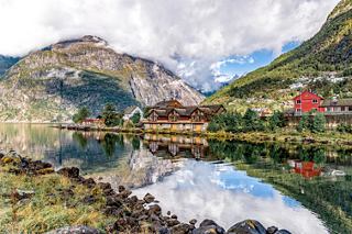 A serene view of Eidfjord reflecting mountains and a colourful building along the coastline | MSC Cruises