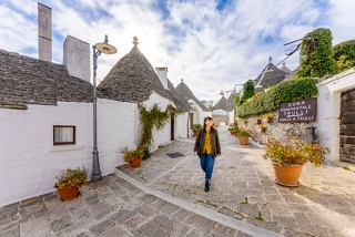 Una mujer camina por una encantadora calle en Alberobello, rodeada de casas trulli tradicionales y plantas vibrantes | MSC Cruceros