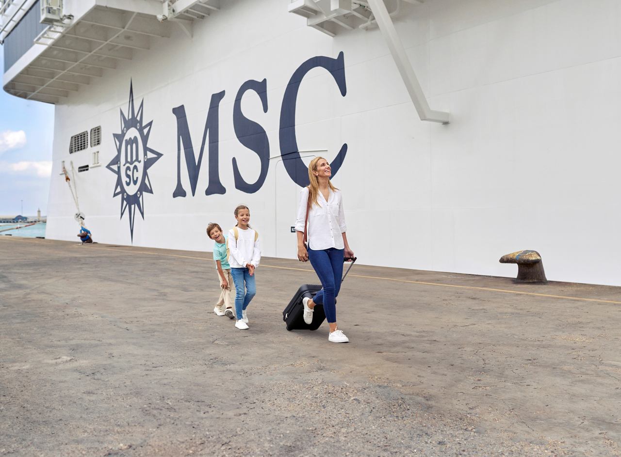 Eine glückliche Familie begibt sich an Bord des Kreuzfahrtschiffes und zieht ihr Gepäck | MSC Cruises