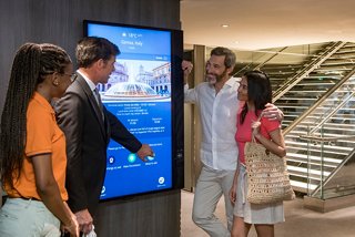 A couple interacts with a staff member at a touchscreen display while exploring MSC Yacht Club options | MSC Cruises