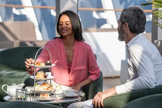A couple enjoys afternoon tea and pastries together in the elegant Top Sail Lounge aboard MSC World Europa | MSC Cruises
