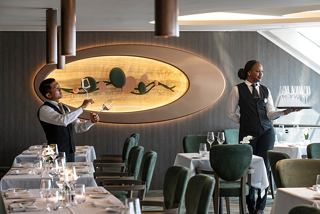 Two attentive waitstaff serve guests in the elegant MSC Yacht Club restaurant aboard MSC World Europa | MSC Cruises