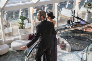 A couple walks hand in hand up the stairs in the elegant Top Sail Lounge with glass walls and stylish decor | MSC Cruises