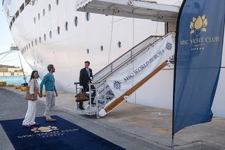A couple is welcomed by crew members as they embark on their MSC cruise, walking on a blue carpet towards the ship | MSC Cruises