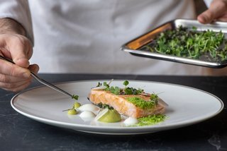 A chef delicately plates a salmon dish with fresh greens, showcasing culinary artistry aboard MSC Yacht Club | MSC Cruises