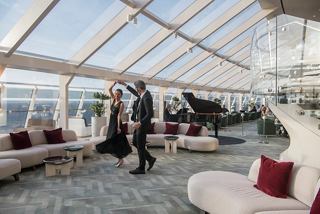 A couple enjoys a moment together in the elegant Top Sail Lounge, overlooking the sea through glass walls | MSC Cruises