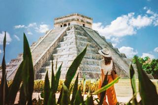 Une femme portant un chapeau se tient près de la pyramide de Kukulkan à Chichen Itza, entourée de verdure luxuriante et de ciels bleus | MSC Croisières