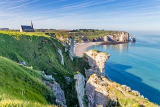 A stunning view of the cliffs and coastline of Etretat, with a church perched on the hill above the beach and sea | MSC Cruises