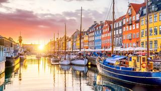 A picturesque view of colourful buildings along a canal in Copenhagen during sunset with boats gently floating | MSC Cruises