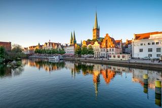 A serene view of Lübeck’s historic skyline reflected in the water, capturing its architectural beauty at sunset | MSC Cruises