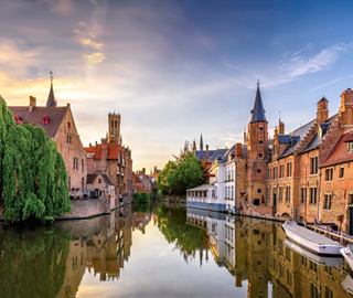 Eine ruhige Kanalszene in Brügge, Belgien, mit charmanter Architektur und historischen Türmen, die sich im Wasser spiegeln | MSC Cruises