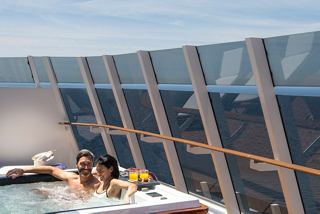 A couple relaxes on a balcony with a cocktail, enjoying the sea view and a whirlpool bath at MSC Yacht Club | MSC Cruises