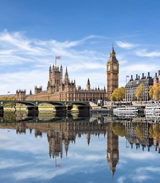 A scenic view of the Houses of Parliament and Big Ben reflected in the River Thames under a clear blue sky | MSC Cruises