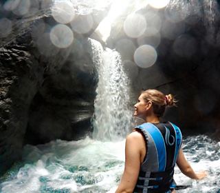 Eine Frau in einer Schwimmweste steht neben einem Wasserfall und umarmt die Schönheit der Natur Dominicas | MSC Cruises