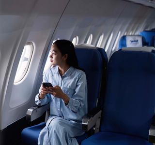 A woman sits by the window on a plane, engaged with her smartphone, ready for an inspiring journey ahead | MSC Cruises