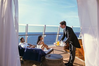 Un couple se détend sur une terrasse pendant qu'un majordome sert des rafraîchissements avec une vue imprenable sur la mer dans le MSC Yacht Club | MSC Cruises