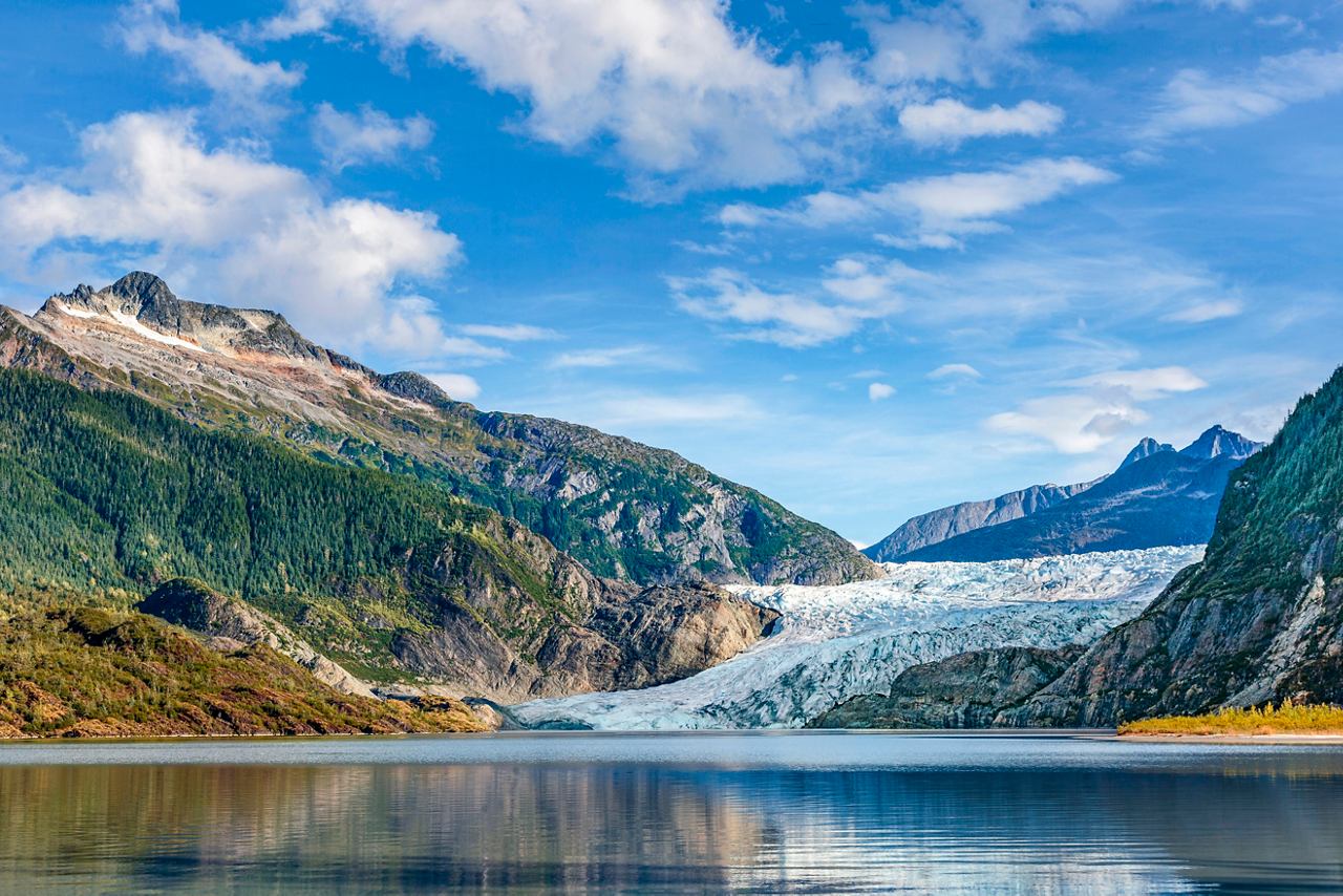 Majestic Mendenhall Glacier reflected in a serene lake surrounded by mountains and a clear blue sky | MSC Cruises