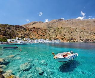 A tranquil scene of a boat on clear turquoise waters with a picturesque town in the background | MSC Cruises