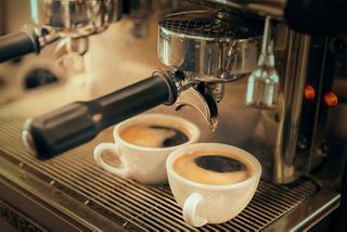 Two espresso cups sit under a coffee machine, showcasing the inviting atmosphere of Caffè Italia on MSC Divina | MSC Cruises