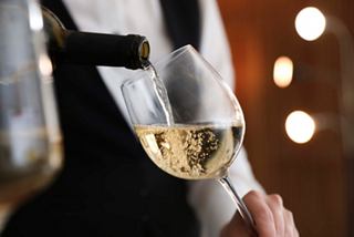 A waiter elegantly holding a gold wine pourer near a bottle in the upscale MSC Yacht Club restaurant | MSC Cruises