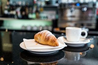 A warm croissant on a plate alongside a cup of coffee in a stylish café setting | MSC Cruises