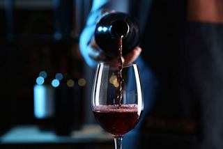 A hand pours red wine into a glass beside an elegant bottle, inviting a moment of relaxation and enjoyment | MSC Cruises