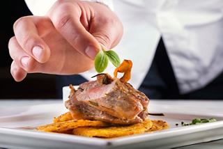 Un chef adornando un plato bellamente presentado con hierbas frescas en un ambiente de restaurante elegante | MSC Cruceros