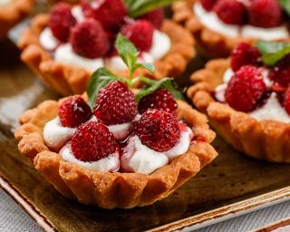 Delicious raspberry tarts topped with cream and mint leaves, served on a wooden platter | MSC Cruises
