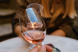 A close-up of a hand holding a glass of rose wine, set on a table in the Top Sail Lounge | MSC Cruises