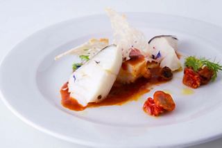 A beautifully presented dish featuring fish with tomato sauce and garnishes, served at The Green Wave Restaurant | MSC Cruises