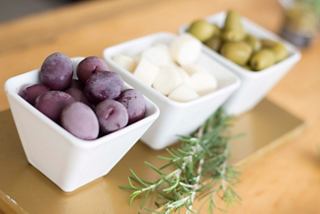 A delightful selection of olives and rosemary served in white bowls on a wooden surface | MSC Cruises