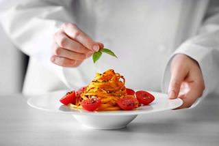 A chef garnishes a plate of pasta with fresh basil and tomatoes in a beautiful dining setting | MSC Cruises