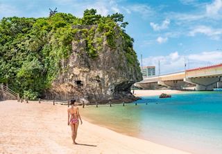 A woman walking along a serene beach with cliffs and turquoise waters in Naha, Japan | MSC Cruises