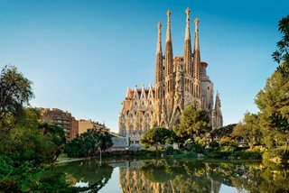The Sagrada Familia stands majestically against a clear sky, surrounded by lush greenery | MSC Cruises
