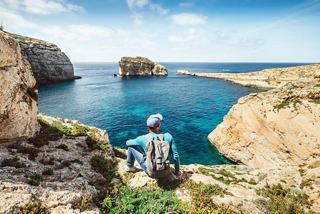 A man enjoys the stunning view of a rocky coastline and blue lagoon in Malta's Mediterranean setting | MSC Cruises