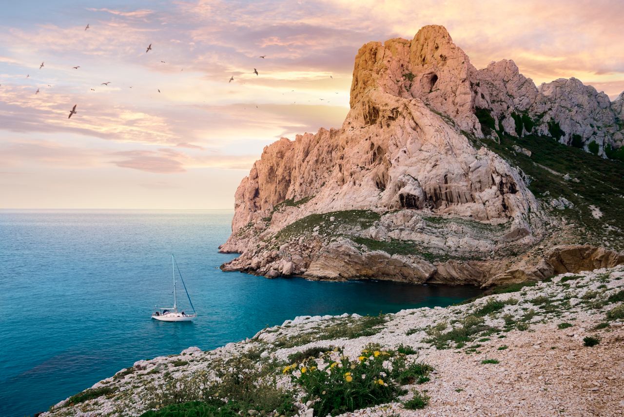 Un impresionante amanecer mediterráneo sobre acantilados rocosos y un barco balanceándose suavemente en el mar cerca de Marsella | MSC Cruises