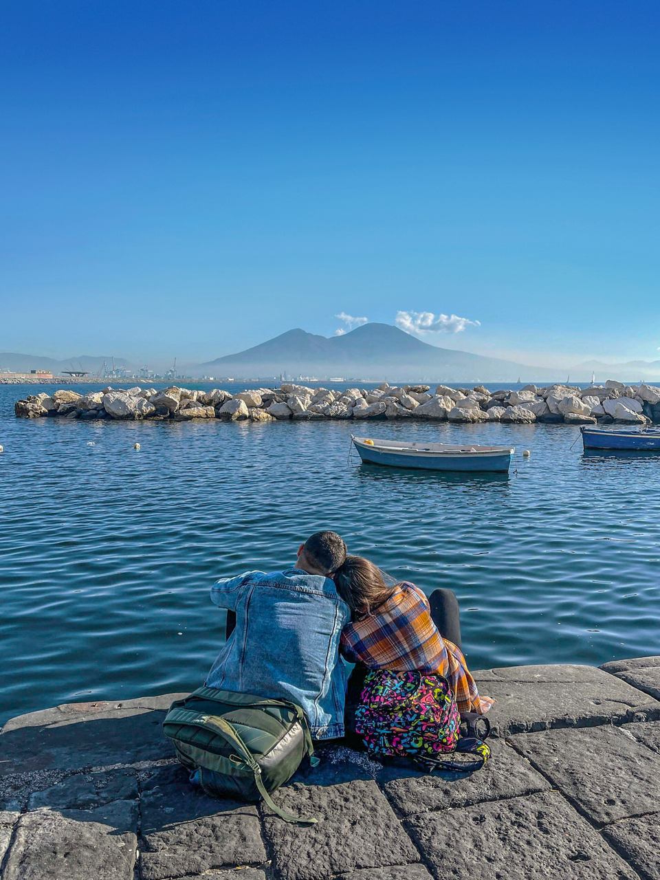 A couple enjoys a serene moment by the sea with Vesuvius in the background, surrounded by boats | MSC Cruises