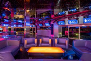 A vibrant entertainment area on MSC Orchestra featuring a dance floor surrounded by seating and colourful lighting | MSC Cruises