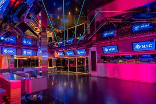 A vibrant dance floor in the R32 Disco on MSC Orchestra, featuring colourful lights and seating areas for guests | MSC Cruises