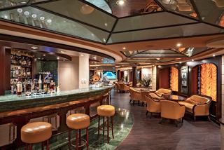 A welcoming lounge with a bar counter, armchairs, and tables for relaxation and socialising onboard MSC Orchestra | MSC Cruises