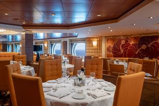 An elegant dining area with tables and chairs, showcasing a warm atmosphere and sea views through the portholes | MSC Cruises