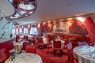 Elegant dining area in the Villa Borghese restaurant with red decor, tables, and portholes overlooking the sea | MSC Cruises