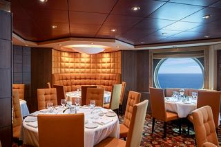 Elegant dining area with a round table and chairs, featuring a porthole view of the sea | MSC Cruises
