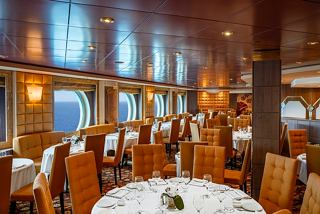 A welcoming dining area with wooden chairs and tables, offering scenic sea views through large porthole windows | MSC Cruises