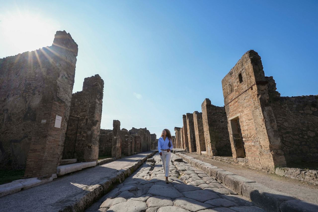 Una mujer camina por un camino rodeado de antiguas ruinas en el sitio arqueológico de Pompeya bajo un cielo despejado | MSC Cruises