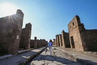 Una mujer camina por un camino rodeado de antiguas ruinas en el sitio arqueológico de Pompeya bajo un cielo despejado | MSC Cruceros
